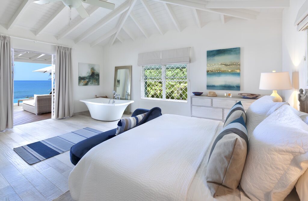 White and blue themed bedroom with a bathtub and a veranda overlooking the sea