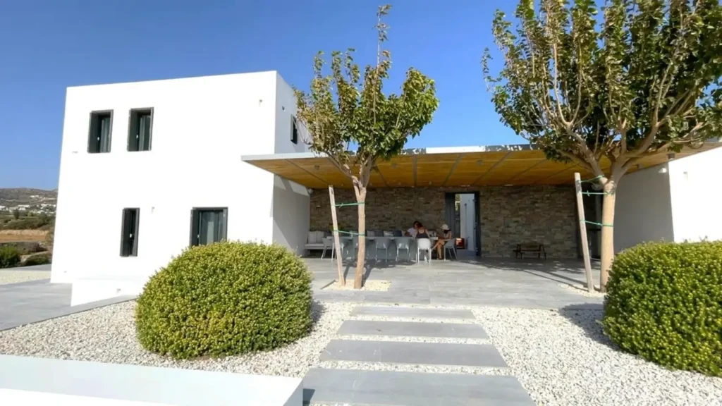 Outdoor dining area of a modern family villa in Paros with shaded seating and a landscaped garden, ideal for a multi-generational vacation