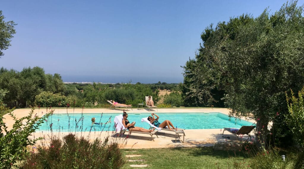 Guests lounging by a private villa pool amidst lush greenery in Puglia