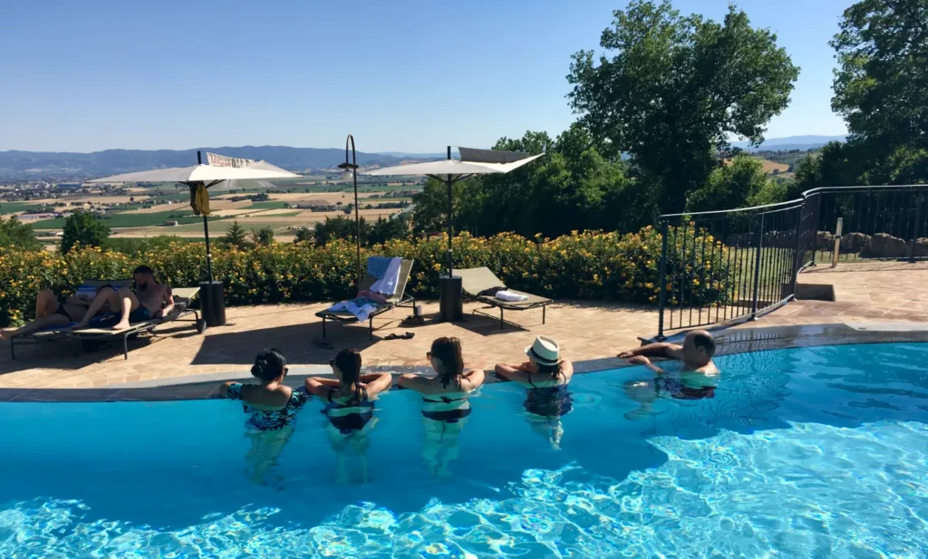 Multi-generational family lounging at the edge of an Italian villa pool with panoramic countryside views, celebrating a family reunion
