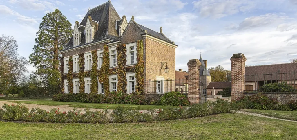 Ivy-covered brick manor with tall slate roof, iron gates and manicured lawn in the countryside.