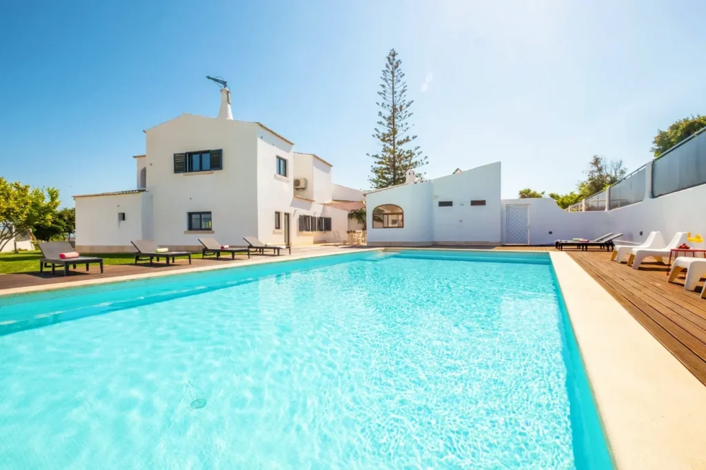 Outdoor pool and sun loungers beside a whitewashed villa under a clear blue sky.