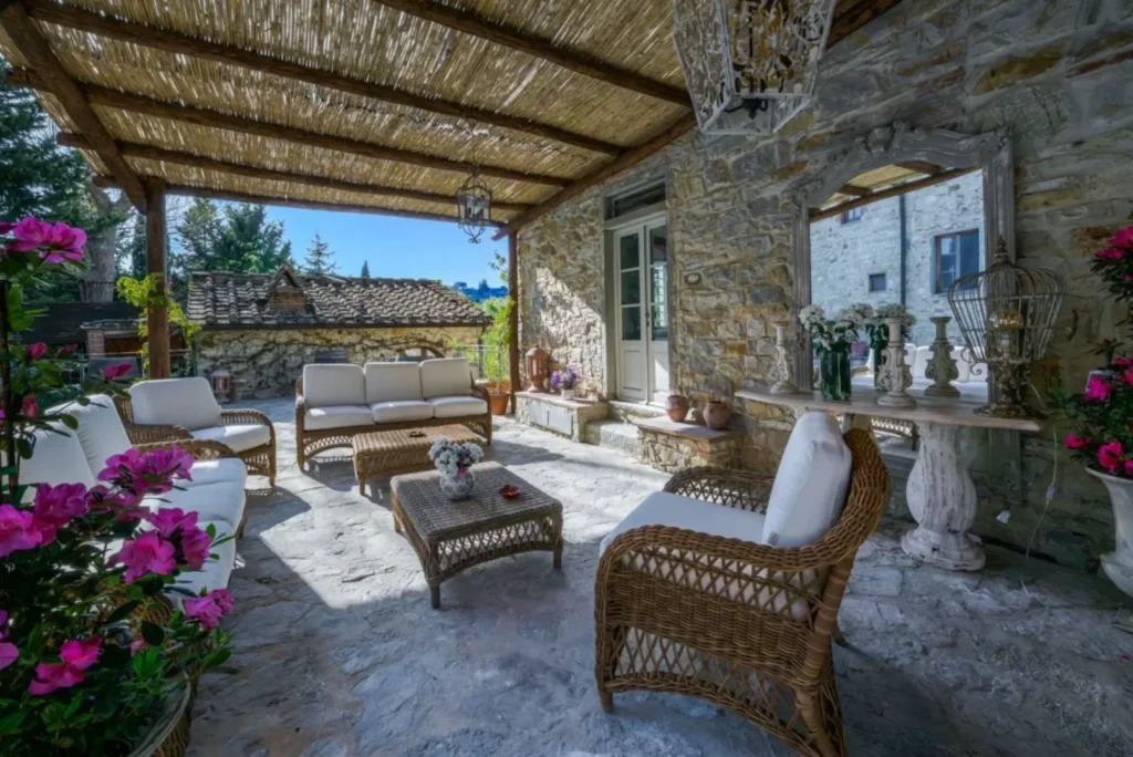 Shaded stone terrace with wicker seating, white cushions and rustic decor.