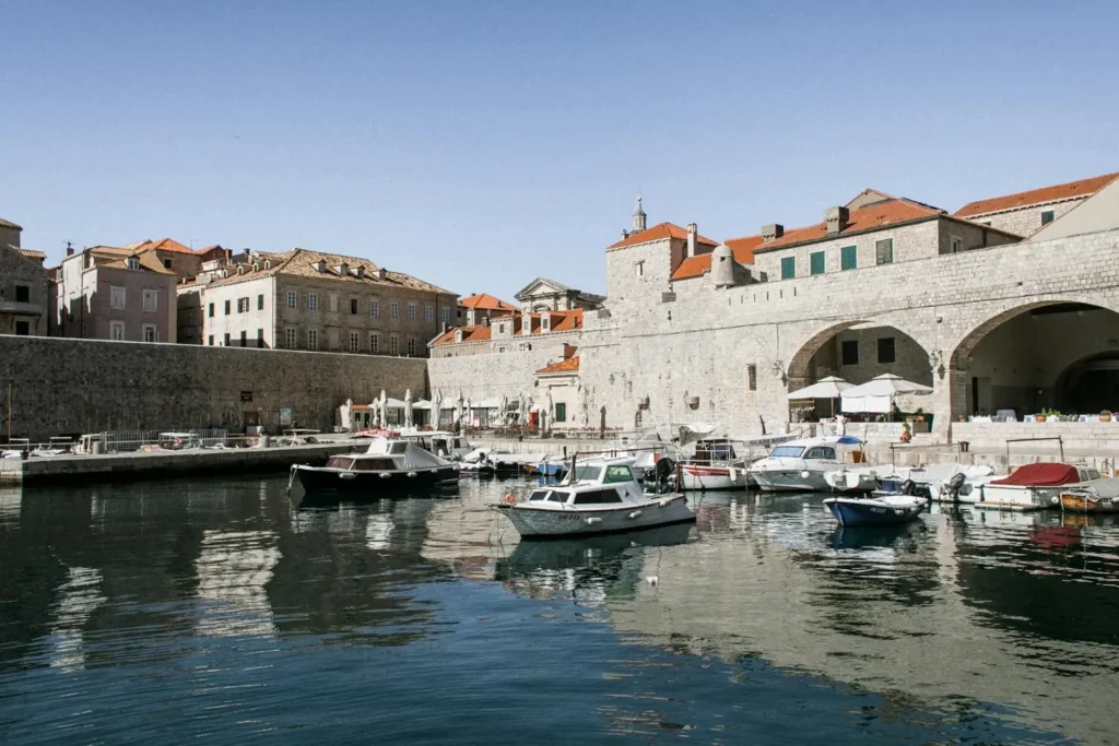 Dubrovnik’s old city port with pale stone walls, terracotta rooftops, and motorboats on the water.