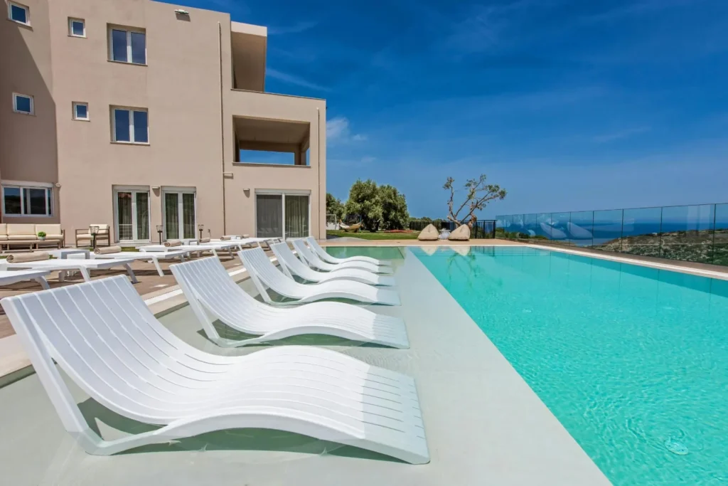 Long outdoor pool with in-water white loungers and sea views beside a modern villa.