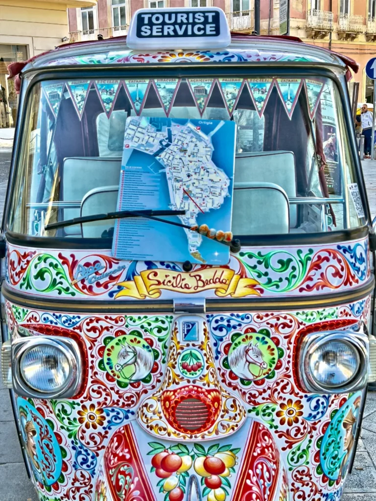 Original photo by paul partridge of a colorfully painted tourist tuk-tuk in siracusa with an ortigia map in the windshield and “tourist service” sign on top.