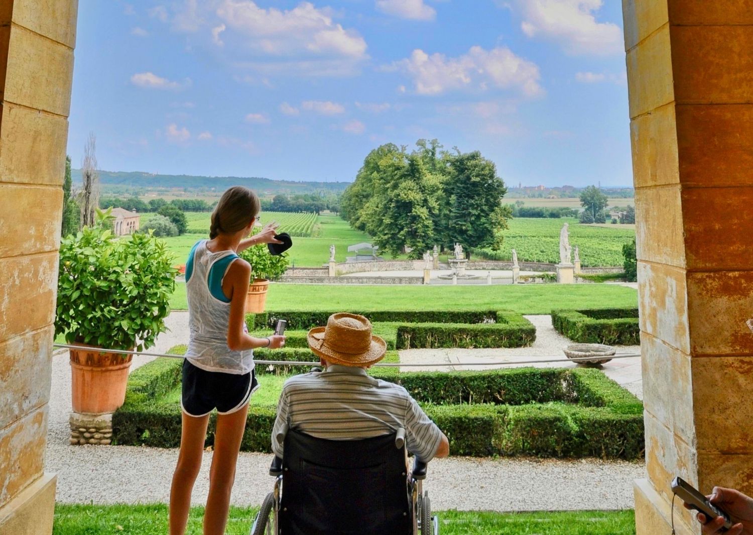 Granddaughter pointing out the Italian countryside to her grandfather in a wheelchair during overseas travel with mobility needs.