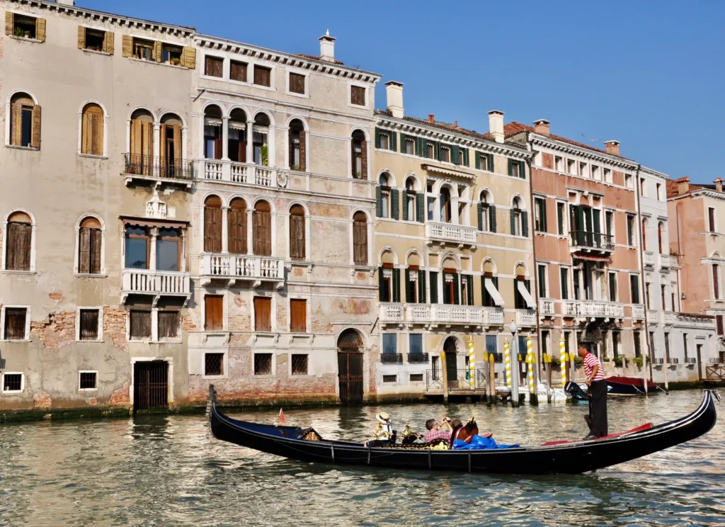 Original photo by paul partridge of a gondolier steering a gondola with passengers along a venice canal lined with weathered buildings.
