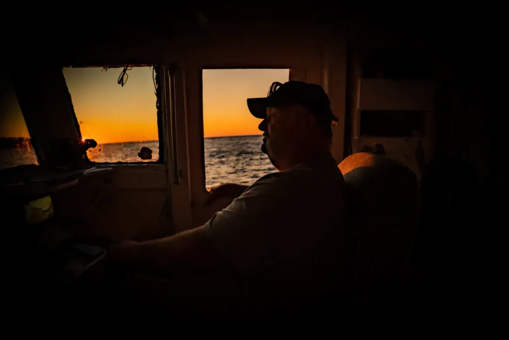 Fishing boat captain returning to harbor at sunset in nova scotia, canada.