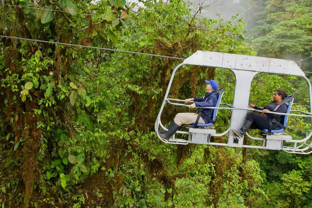 Two travelers ride high above the trees on an open-air canopy chair in ecuador’s lush jungle.
