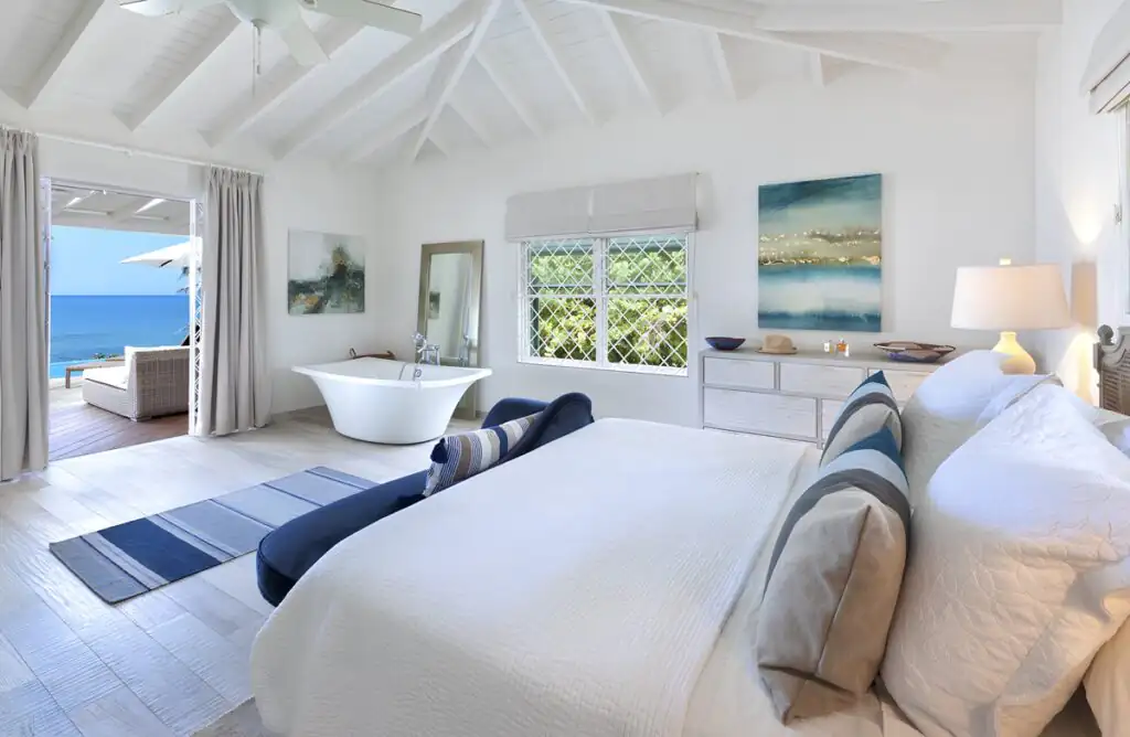 White and blue themed bedroom with a bathtub and a veranda overlooking the sea