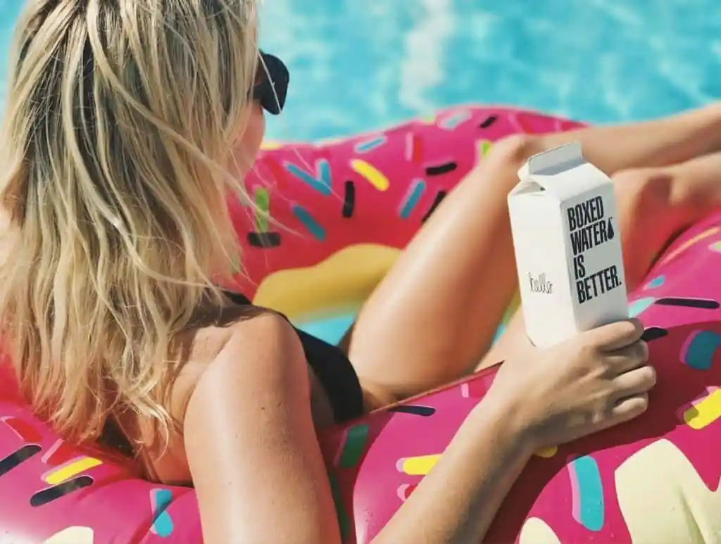 A woman on a swim ring in a pool, holding boxed water