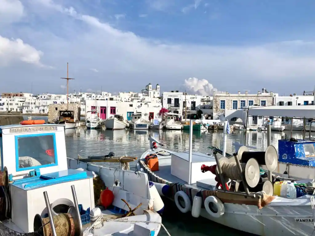 Original photo by paul partridge of fishing boats moored in the greek island harbor of naousa, with whitewashed buildings and colorful doors lining the waterfront.