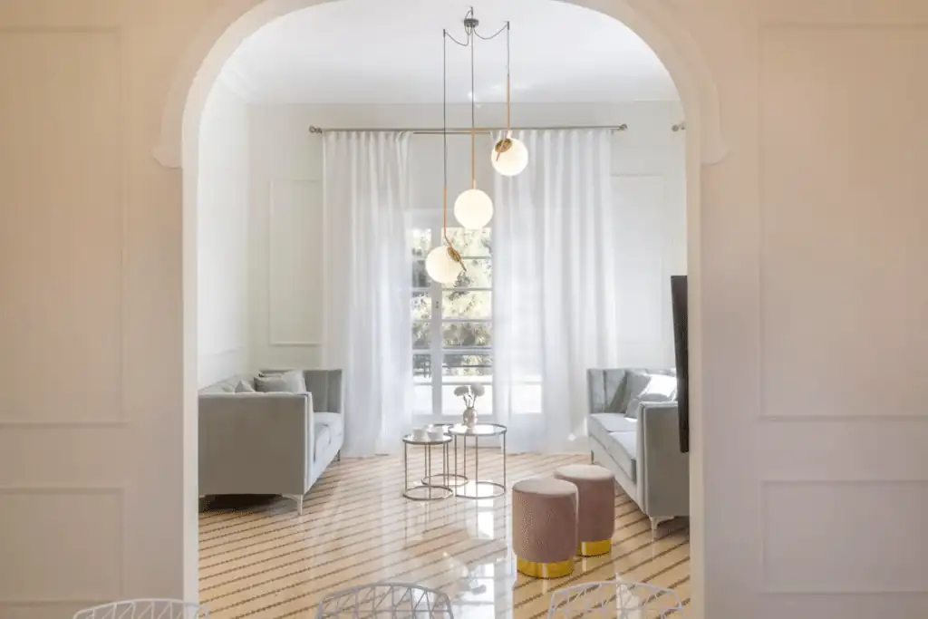 Bright living room with an arched entryway, white walls and curtains, modern grey sofas, and a striped wood floor in a private villa in glyfada, greece.