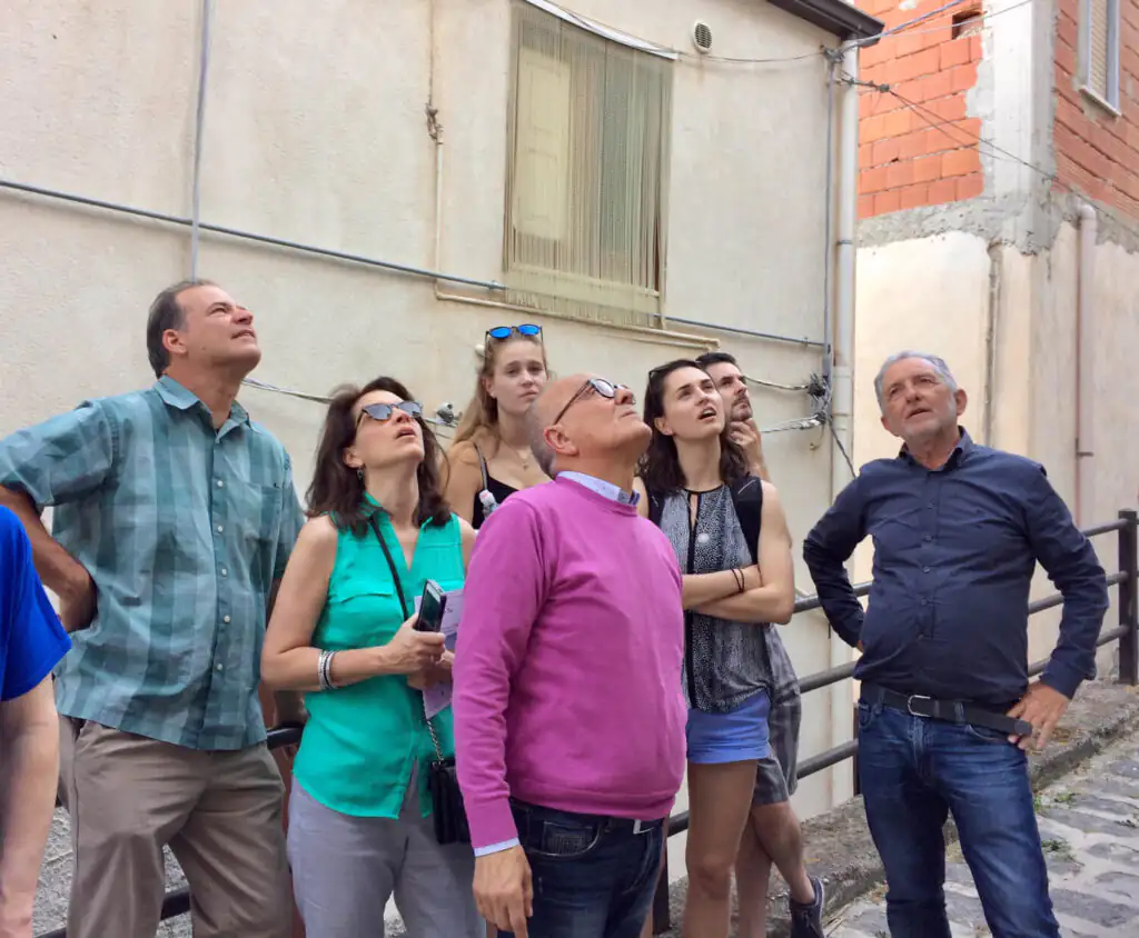 A multi-generational American family on a tour with the Mayor of Cammarata, Sicily, pausing to observe local buildings tied to their Italian roots.