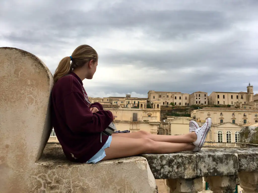 A teenage girl looks out over the rooftops of Noto during a trip exploring family roots in Sicily.