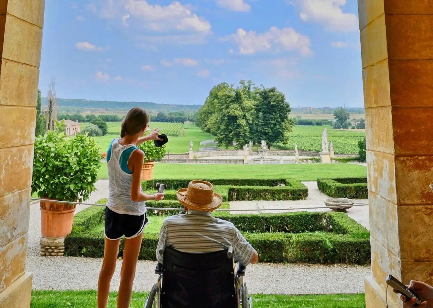 Granddaughter pointing out the Italian countryside to her grandfather in a wheelchair during overseas travel with mobility needs.