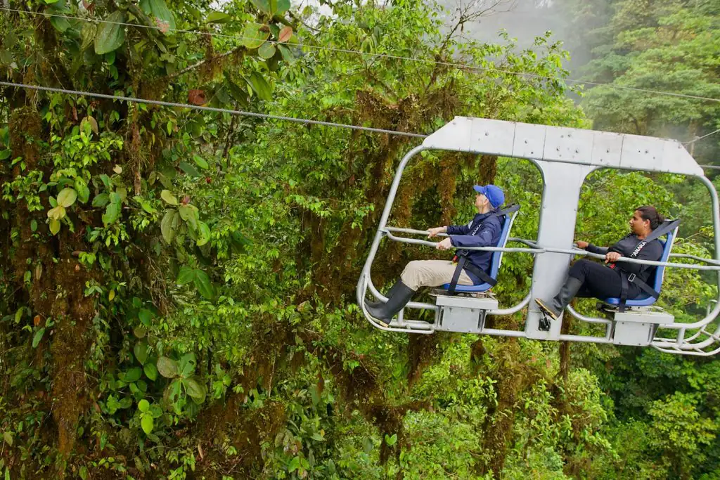 Two travelers ride high above the trees on an open-air canopy chair in ecuador’s lush jungle.